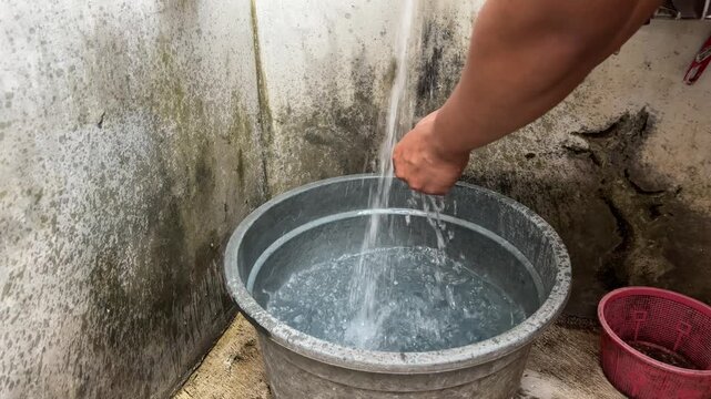 Person Washing Hands in a Bucket in a Rustic Setting.