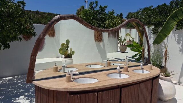 Rustic wooden outdoor sink vanity with an arched canopy and green plants at a beach club resort in Cesme Turkey