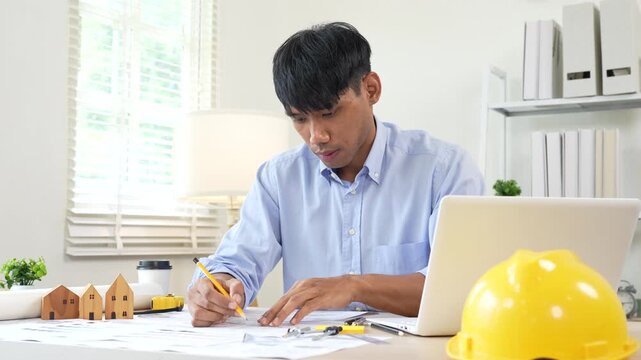 Architect reviewing construction plans at a modern office desk with blueprints, laptop, and engineering tools for a building project.