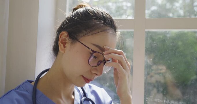 Female healthcare professional wearing scrubs and a stethoscope holding her forehead, expressing stress, fatigue, burnout, and mental pressure in a clinical setting.