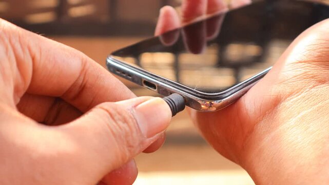 Connecting Audio. Asian man's hand Plugging Wired Earphones into a Smartphone.