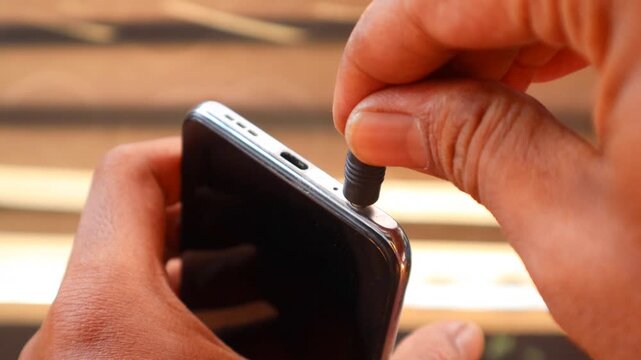 Connecting Audio. Asian man's hand Plugging Wired Earphones into a Smartphone.