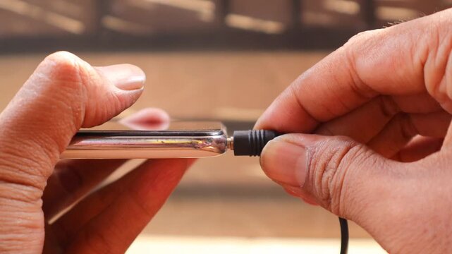 Connecting Audio. Asian man's hand Plugging Wired Earphones into a Smartphone.