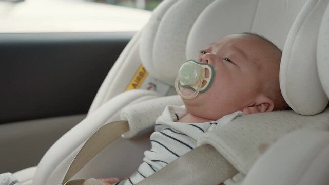 Baby sleeps peacefully in car seat. Soft pacifier rests against their lips. White seat cushion supports their tiny body. Calm, serene expression shows deep rest. Ideal for parenting, travel