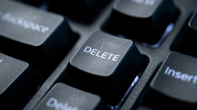Close up of a computer keyboard's DELETE key illuminated by subtle lighting, highlighting the tactile nature of the button