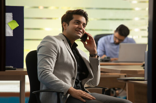 AN OFFICE EXECUTIVE TALKING TO CLIENT OVER PHONE WITH COLLEAGUE WORKING IN THE BACKGROUND 