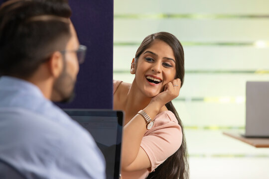 A HAPPY EXECUTIVE TALKING TO HER COLLEAGUE WHILE SITTING IN HER CUBICLE