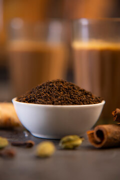 Close up of a bowl filled with tea leaves with spices around it