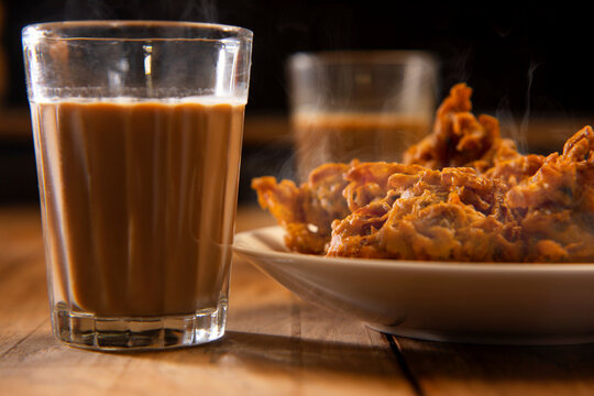 Tea glass kept in front of a plate filled withpakoras on a table