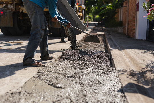 Construction worker using a hoe tool to spread fresh wet concrete from a mixer truck.