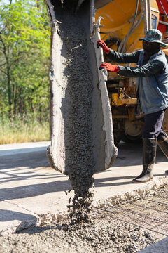 Construction worker with wet concrete flows onto a foundation for road repaving.