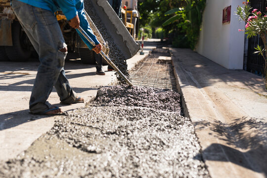 Construction worker using a hoe tool to spread fresh wet concrete from a mixer truck.