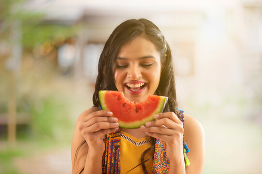  A HAPPY YOUNG WOMAN ENJOYING A SLICE OF WATERMELON