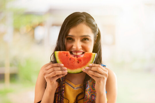 A YOUNG WOMAN HAPPILY LOOKING ABOVE WHILE EATING WATERMELON