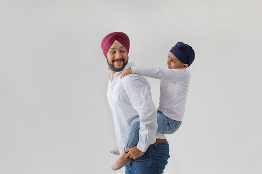 A SIKH FATHER CARRYING SON ON BACK AND LOOKING AT HIM
