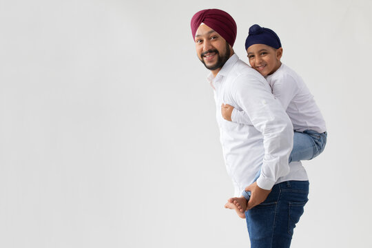 A SIKH FATHER CARRYING HIS SON ON HIS BACK SIMILING AND POSING