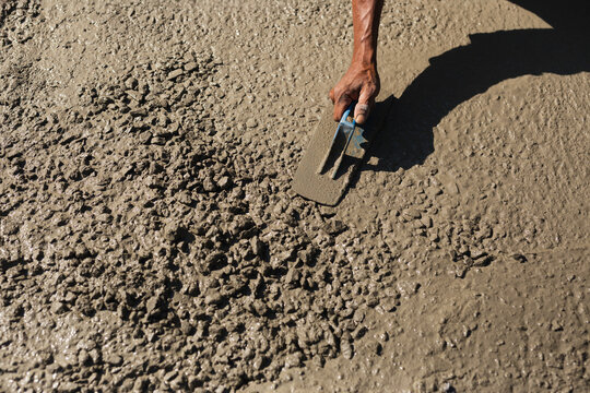Construction worker using a trowel to smooth fresh gravel mixed cement on a road surface.
