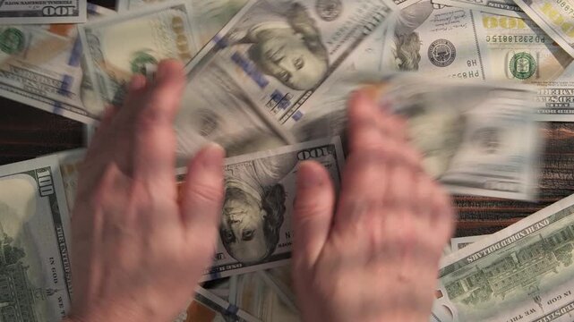 Man's hands collecting cash 100 dollar bills from table, rake in money