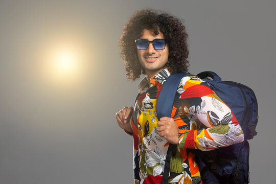 A STYLISH YOUNG MAN WEARING GOGGLES AND HOLDING BAG SMILING AT CAMERA