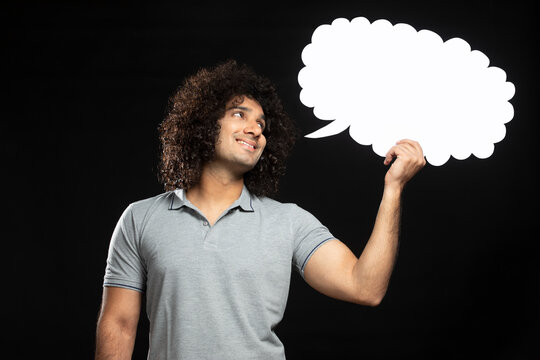 A YOUNG MAN WITH CURLY HAIR HOLDING THOUGHT BUBBLE AND LOOKING AT IT