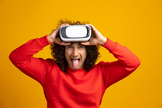 A YOUNG MAN WITH CURLY HAIR HOLDING VR DEVICE AND PLAYFULLY POSING