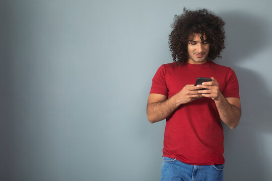 A CURLY HAIRED YOUNG MAN STANDING AND USING MOBILE PHONE