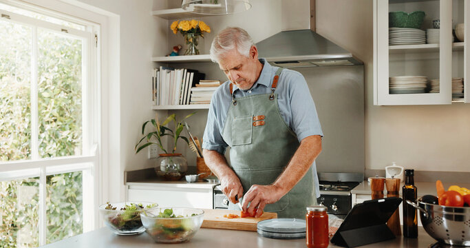 Senior, man and cooking in kitchen with vegetables, tablet and healthy food for retirement wellness. Elderly person, meal prep and chop in home with ingredients, nutrition and tech for lunch recipe.