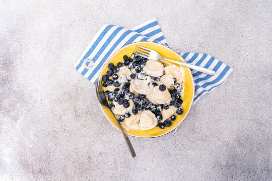 Overhead view of a plate of Traditional Ukrainian dumplings stuffed with cottage cheese (varenyky), sour cream and blueberries on a table with a napkin and cutlery