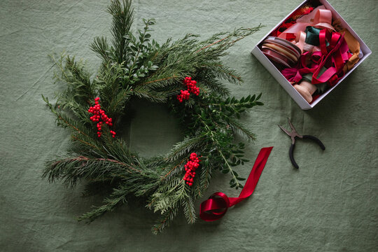 Overhead view of a handmade Christmas wreath and a box of assorted ribbons with a pair of pliers on a table