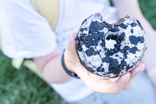 Overhead view of a teenage boy sitting in a park eating a chocolate donut with vanilla frosting