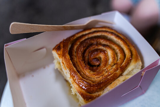 Close-up of a cinnamon roll in a cardboard box with a wooden fork