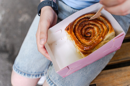 Close-up overhead view of a teenage boy sitting in a park eating a cinnamon roll in a cardboard box