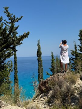 Rear view of a Woman in a white dress taking a photo of the Ionian Sea, Lefkada, Ionian islands, Greece
