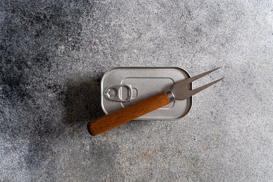 Close-up overhead view of an unopened tin of canned fish and a fork on a concrete worktop