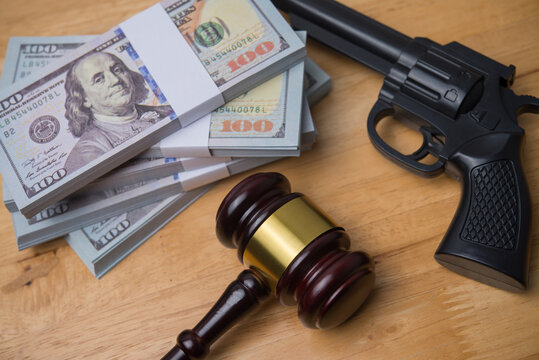 Judge gavel, a handgun and US dollar bill banknotes on wooden table background in courtroom. Crime and punishment, illegal, law, justice, corruption, dirty money, money laundering and so on concept.