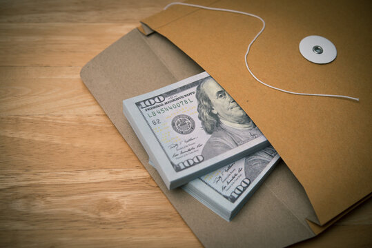 Close up US bill banknotes in the opened paper bag envelope with lock string ring on wooden table. Graft money, bribery, corruption in the government, dirty money and so on concept.