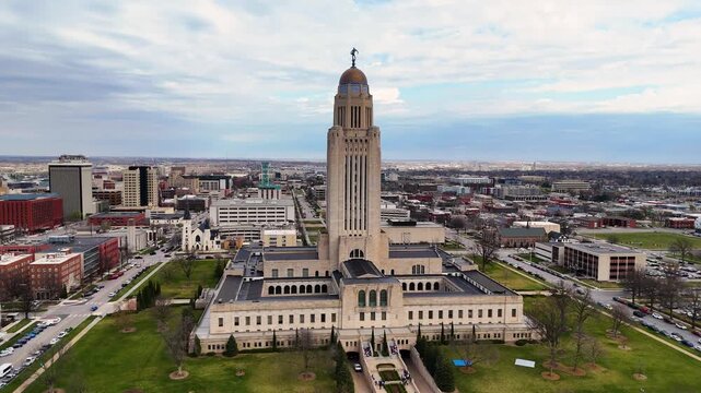 Majestic drone footage of the Nebraska State Capitol in Lincoln, Nebraska, USA, featuring the iconic government tower topped with The Sower statue, surrounded by downtown streets 