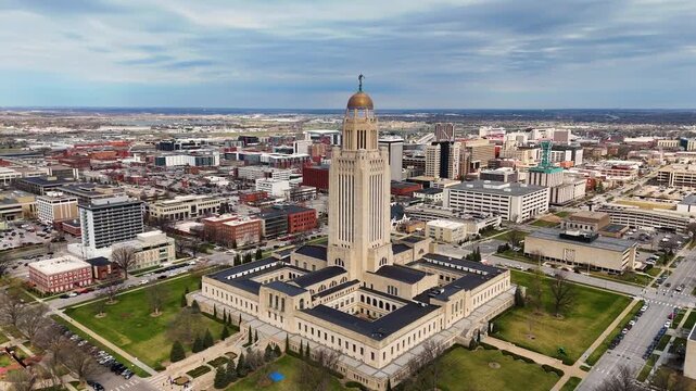 Majestic drone footage of the Nebraska State Capitol in Lincoln, Nebraska, USA, featuring the iconic government tower topped with The Sower statue, surrounded by downtown streets 