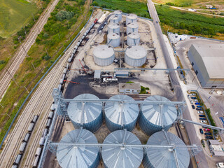 Large storage facility with silos and railway tracks located in an industrial area near a highway at midday © DSMT