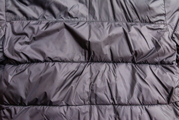Black quilted puffer jacket fabric texture background with copy space. Puffy winter clothing material background with space for text. Minimalist dark nylon textile banner. horizontal stitched baffles. © ARVD73