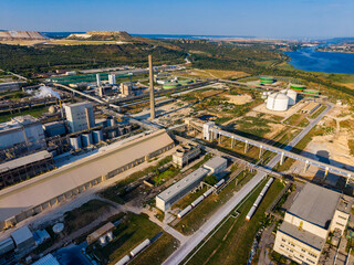 Fototapeta premium Industrial area with factories and storage tanks near river and hills in clear weather