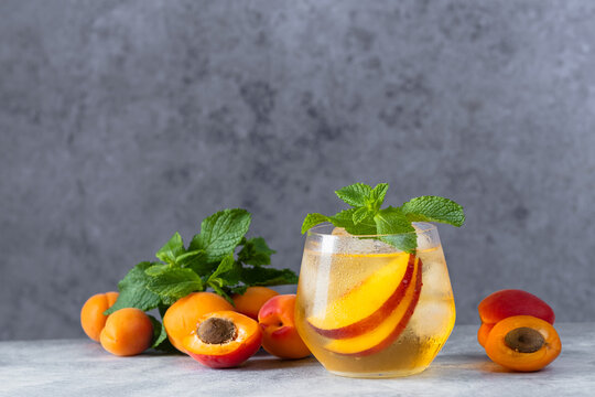 One glasses refreshing iced tea with peach and mint on a wooden background. Each glass contains slices of fruit and mint leaves.