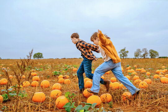 Teenage brother and child girl running through pumpkin patch together