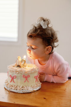 Toddler girl blows out the candle on her second birthday cake