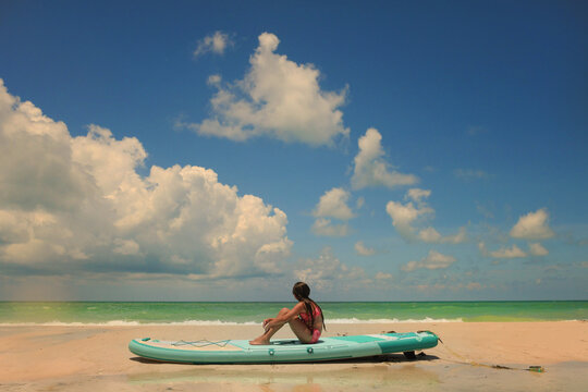 Young woman sitting on paddleboard on beach