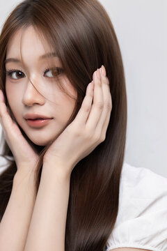Korean style beauty portrait of lovely young Asian woman with natural glam makeup and sleek brown hair against studio backdrop, Highlighting healthy nails, clear skin, and a Korean beauty aesthetic.