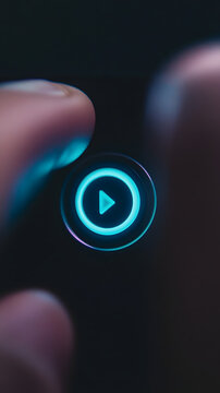 Finger presses a glowing circular play button that features a bright blue neon light indicator on a dark electronic device interface, suggesting digital interaction and media control.