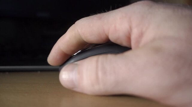 Close-up of a Hand Reaching to Grab a Black Wireless Computer Mouse on a Desk