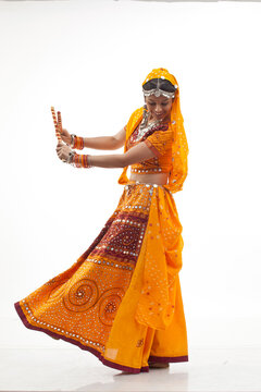 Happy young woman in chaniya choli performing Dandiya Raas against white background