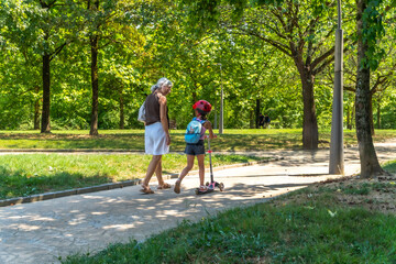 Obraz premium Grandmother and granddaughter walking with scooter in park